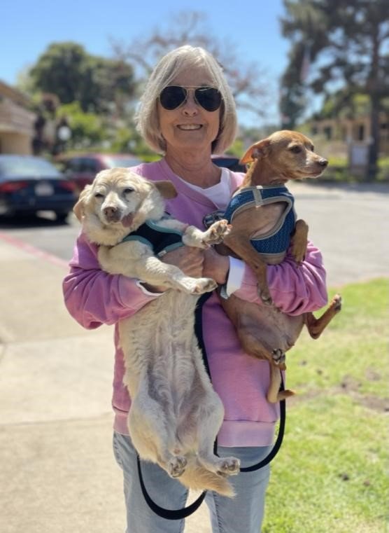 Diane, a Tender Hearts Dog Rescue teammate, holding her two dogs and standing in a driveway.