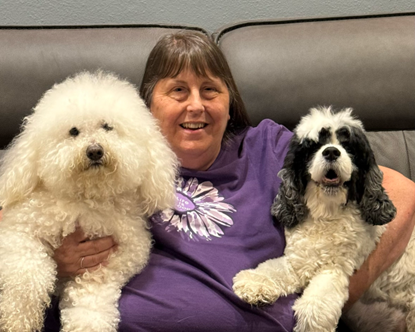 Laurie, a Tender Hearts Dog Rescue teammate, and her two dogs sitting on a faux leather couch.